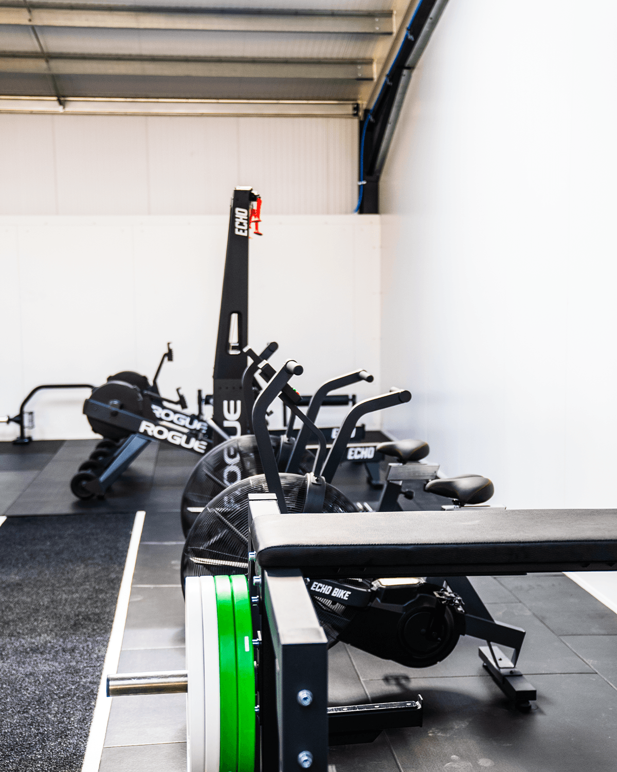 Close-up of the Rogue rower, Echo bike, and bench set up in the conditioning area.