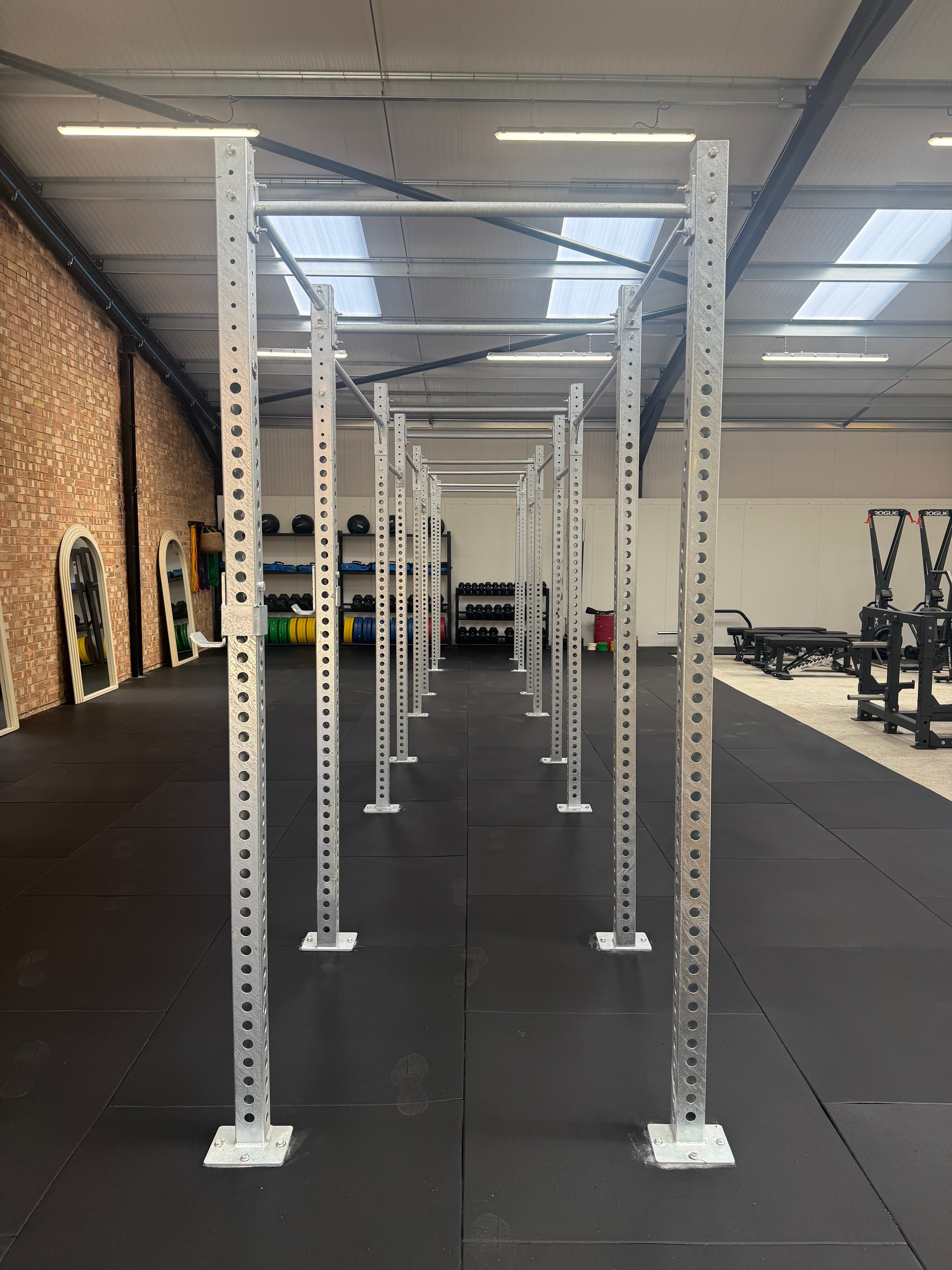 The Magni Fitness gym floor: a run of galvanised lifting rigs down the centre, mirrors along the brick wall, and machines at the far end.